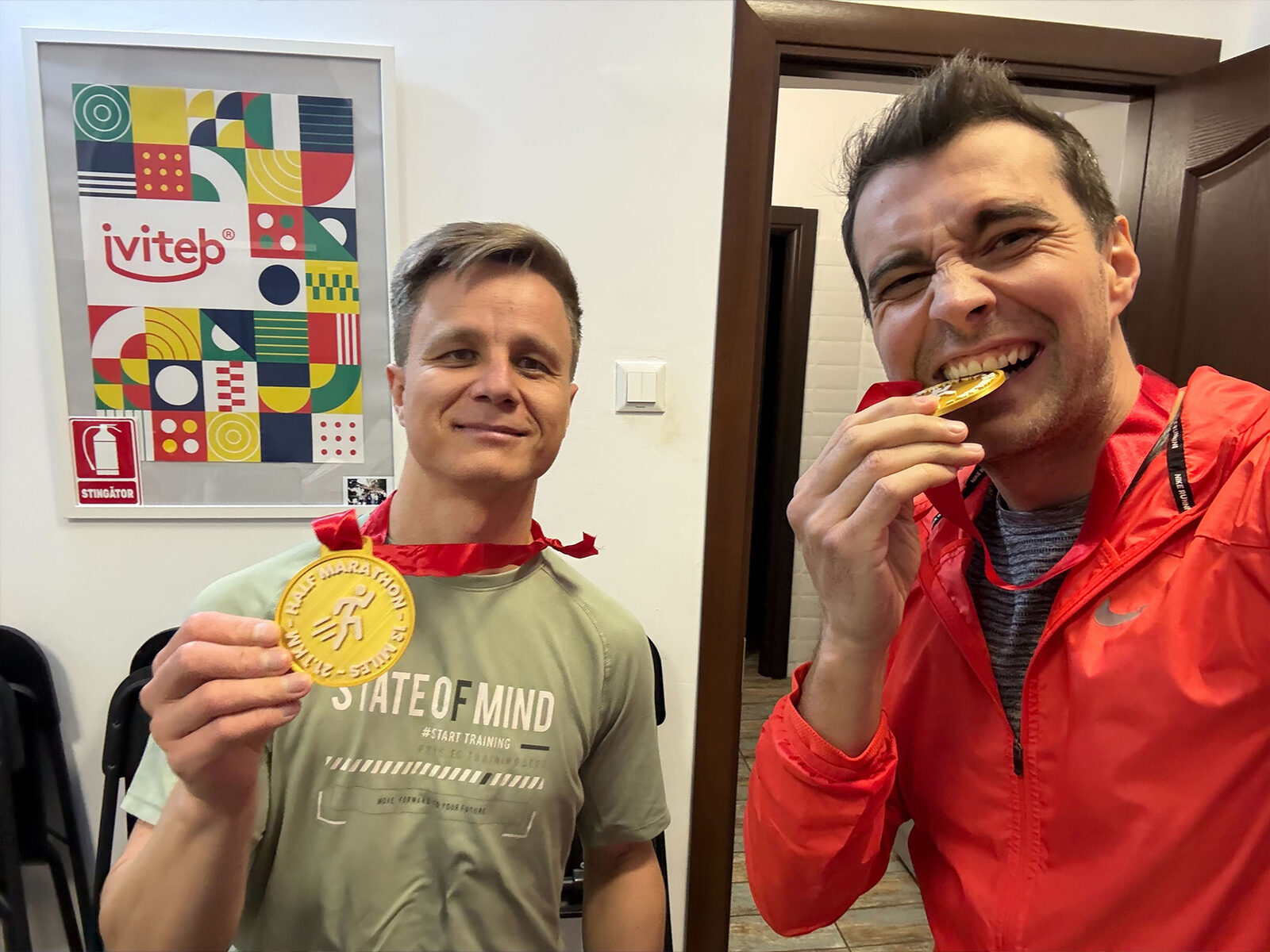 Two of the team with half-marathon medals in front of the iviteb poster